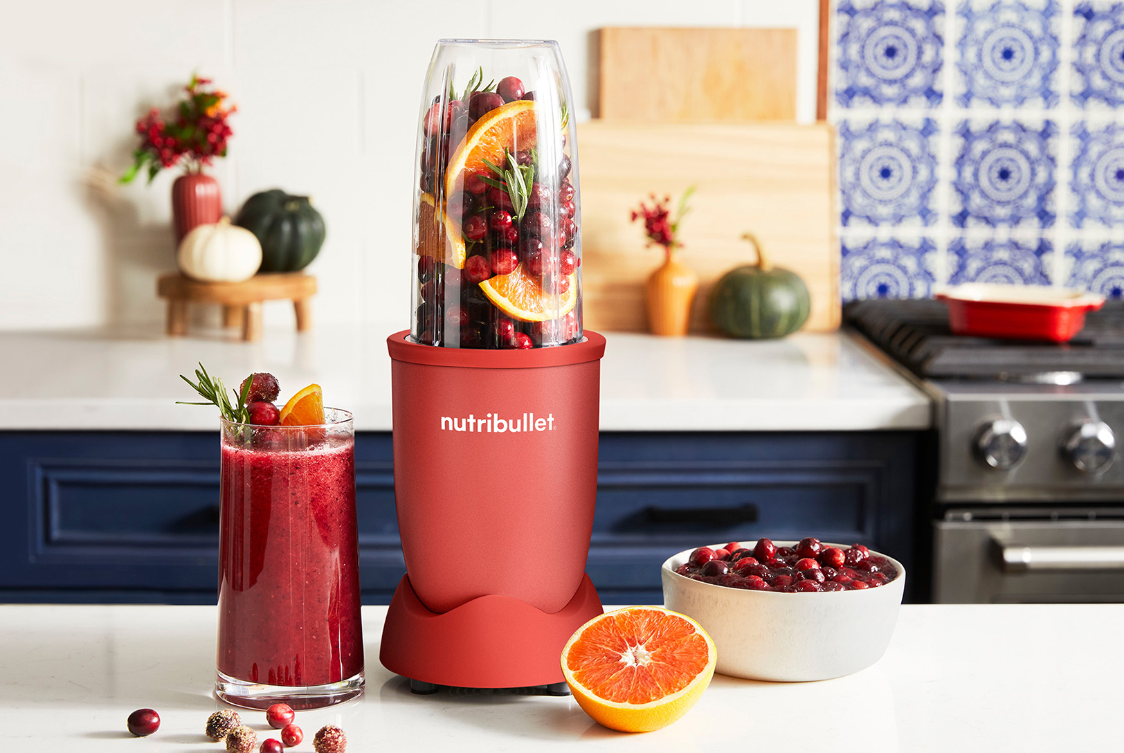 nutribullet blender with a glass of cranberry smoothie and a bowl of cranberries on a kitchen counter